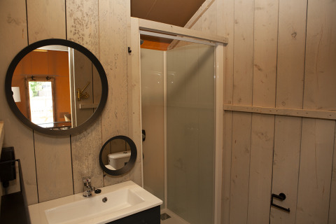 Baño en Safaricottage XL con ducha, espejos redondos y lavabo en Holiday Park Sallandshoeve, Países Bajos.