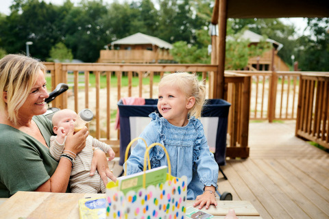 Famille profitant d’un moment sur la terrasse d’une Safaricottage XL au Holiday Park Sallandshoeve, Pays-Bas.