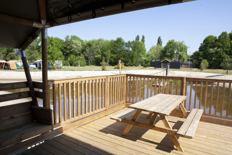 Terraza de madera con mesa de picnic junto al lago en Safaricottage XL, Holiday Park Sallandshoeve, Países Bajos.