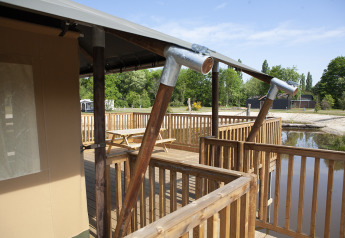 Vue depuis la terrasse d’une tente safari avec rambarde en bois, au bord de l’eau au Holiday Park Sallandshoeve.