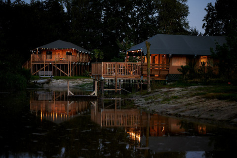 Tiendas de safari iluminadas junto al lago en Holiday Park Sallandshoeve, Países Bajos, al anochecer.