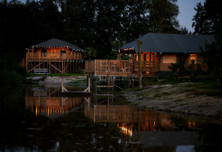 Tentes safari éclairées au bord du lac au Holiday Park Sallandshoeve aux Pays-Bas, photographiées le soir.
