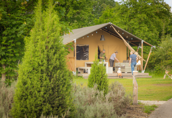 Gezin geniet buiten voor een safaritent bij Vakantiepark Sallandshoeve in Nederland, omgeven door groen.