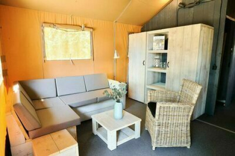 Sala de estar de una tienda safari en Holiday Park Sallandshoeve, Países Bajos, con sofá y silla de mimbre.