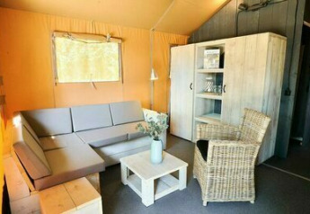 Sala de estar de una tienda safari en Holiday Park Sallandshoeve, Países Bajos, con sofá y silla de mimbre.