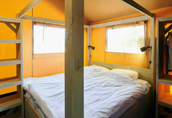 Interieur van een safaritent met tweepersoonsbed en houten frame bij Vakantiepark Sallandshoeve in Nederland.