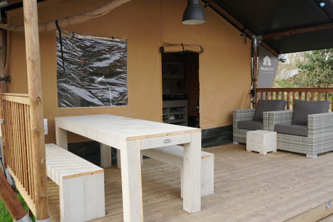 Véranda extérieure avec table, banc et fauteuils devant une tente safari au parc Sallandshoeve, Pays-Bas.