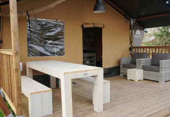Véranda extérieure avec table, banc et fauteuils devant une tente safari au parc Sallandshoeve, Pays-Bas.
