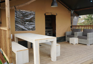 En udendørs veranda med spisebord, bænk og loungestole foran en safaritelt på Sallandshoeve, Holland.