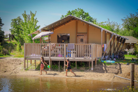 Niños juegan junto al agua frente a una tienda safari de lujo en Holiday Park Sallandshoeve, Países Bajos.