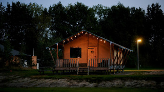 Luxe safaritent aan het water bij Holiday Park Sallandshoeve in Nederland, sfeervol verlicht ’s avonds.
