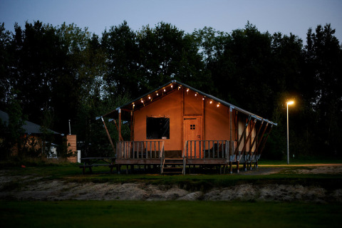 Luxury safari tent on the waterfront at Holiday Park Sallandshoeve in the Netherlands, lit at dusk.