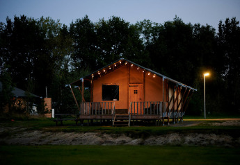 Tienda safari de lujo frente al agua en Holiday Park Sallandshoeve, Países Bajos, iluminada al anochecer.