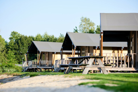 Tiendas safari de lujo junto al agua en Holiday Park Sallandshoeve, Países Bajos, con bancos de picnic.