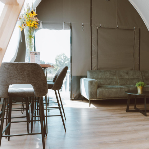 Interieur van de Big Oak Tent bij Holiday Park Sallandshoeve, Nederland, met sofa en eetgedeelte.