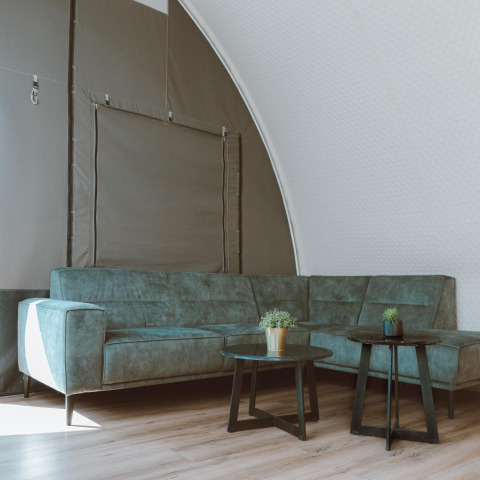 Moderne zithoek in de Big Oak Tent bij Holiday Park Sallandshoeve, met groene zetel en tafels.