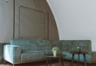 Moderne zithoek in de Big Oak Tent bij Holiday Park Sallandshoeve, met groene zetel en tafels.