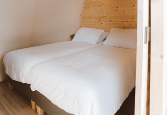 To enkeltsenge med hvide lagner i Big Oak Tent på Holiday Park Sallandshoeve, Holland, trævæg bagved.