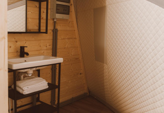 Moderne wastafel met spiegel, houten bekleding en gewatteerde muren in de Big Oak Tent, Holiday Park Sallandshoeve, Nederland.
