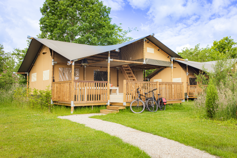 Tienda safari Ranger Lodge en Holiday Park Sallandshoeve, Países Bajos, con porche de madera y bicicletas.