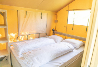 Vista interior de una tienda safari Ranger Lodge con cama doble y ventanas en Holiday Park Sallandshoeve.