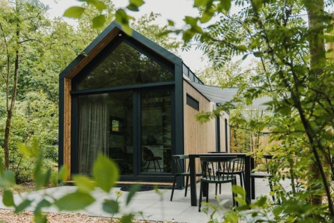 Modern tiny house at Camping Si-Es-An in the Netherlands, surrounded by trees with a patio seating area.