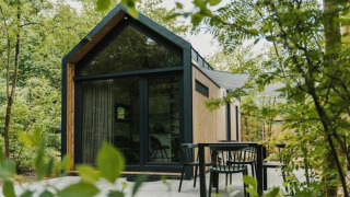 Moderne tiny house ved Camping Si-Es-An i Holland, omgivet af grønne træer og udendørs siddeplads.