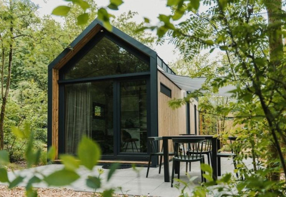 Moderne tiny house op Camping Si-Es-An in Nederland, omgeven door bomen en met buitenterras.