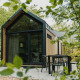 Modern tiny house at Camping Si-Es-An in the Netherlands, surrounded by trees with a patio seating area.