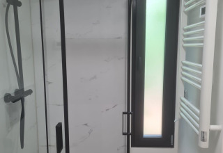 Moderne douche met glazen wand, regendouche, zwart frame en smal raam in een tiny house badkamer.