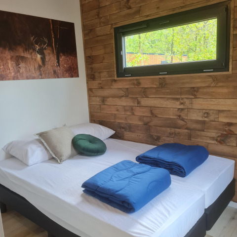 Chambre douillette du Tiny House I au Camping Si-Es-An, Pays-Bas, mur en bois et linge bleu.