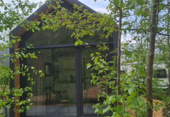 Casa diminuta llamada Tiny house l en Camping Si-Es-An en Países Bajos, rodeada de árboles verdes.