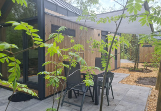 Terraza con mesa y sillas frente a una tiny house en Camping Si-Es-An, Países Bajos, rodeada de naturaleza.