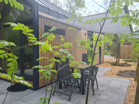 Patio with table and chairs outside a tiny house at Camping Si-Es-An in the Netherlands, surrounded by greenery.