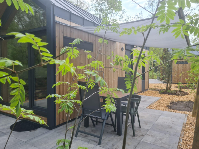 Patio with table and chairs outside a tiny house at Camping Si-Es-An in the Netherlands, surrounded by greenery.