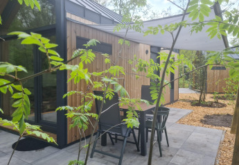 Udendørs terrasse med bord og stole foran et træbeklædt tiny house ved Camping Si-Es-An i Holland.