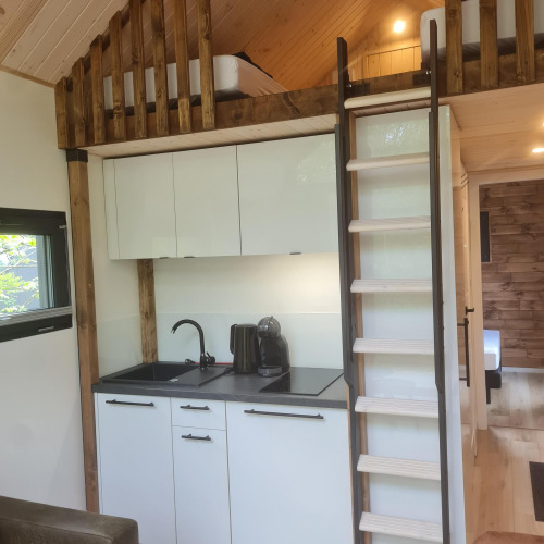 Modern tiny house kitchen area with loft bed and wooden ladder at Camping Si-Es-An in the Netherlands.