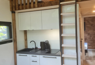 Modern tiny house kitchen area with loft bed and wooden ladder at Camping Si-Es-An in the Netherlands.