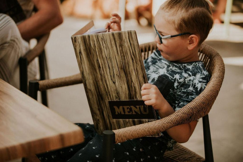 Un niño sentado en una silla lee un gran menú en Tiny house l en Camping Si-Es-An en los Países Bajos.