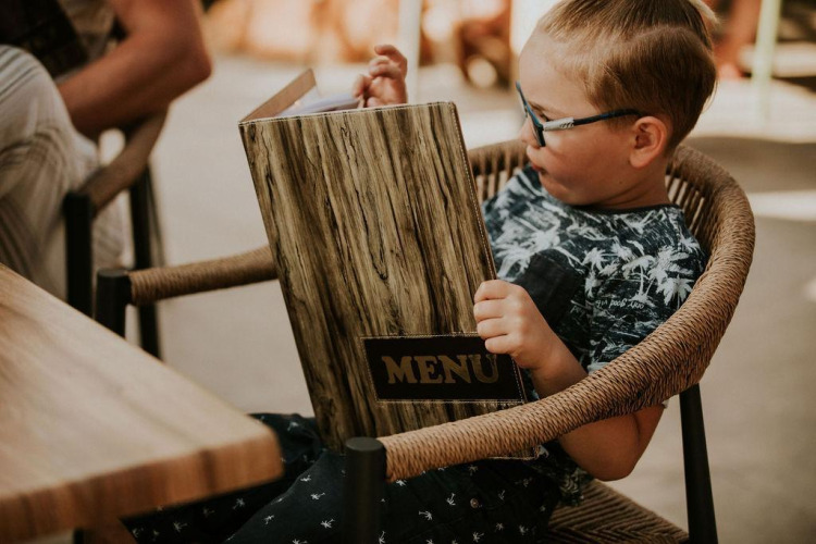 A child sits in a chair reading a large menu at Tiny house l at Camping Si-Es-An in the Netherlands.