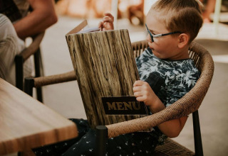 Un enfant assis sur une chaise lit un grand menu au Tiny house l du Camping Si-Es-An aux Pays-Bas.