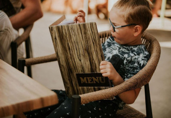 Un niño sentado en una silla lee un gran menú en Tiny house l en Camping Si-Es-An en los Países Bajos.
