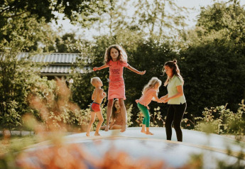 Niños y una adulta juegan felices en una colchoneta inflable en el jardín de un alojamiento glamping.