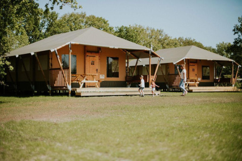 Safari tents at Camping Si-Es-An in the Netherlands with a family and kids playing in front of the lodges.