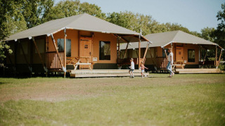 Tende safari al Camping Si-Es-An nei Paesi Bassi con una famiglia e bambini che giocano davanti ai lodge.