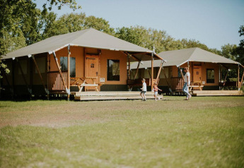 Safari tents at Camping Si-Es-An in the Netherlands with a family and kids playing in front of the lodges.