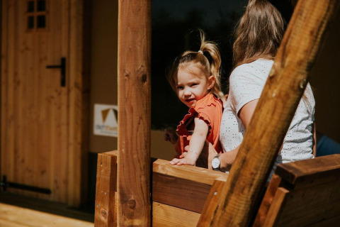 Kleines Mädchen mit Erwachsenem auf Holzveranda im Safari-Zelt, Camping Si-Es-An, Niederlande, sonnig.