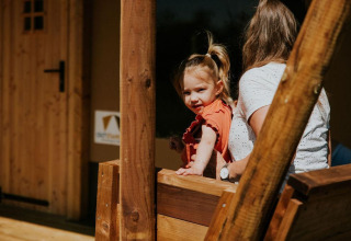 Niña pequeña con adulto en el porche de madera de una tienda Safari en Camping Si-Es-An, Países Bajos, soleado.