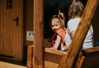 Young girl with adult on wooden porch of a safari tent at Camping Si-Es-An, Netherlands, sunny afternoon.