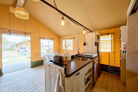 Interior de la tienda safari en Camping Si-Es-An, Países Bajos, con cocina y zona de comedor.